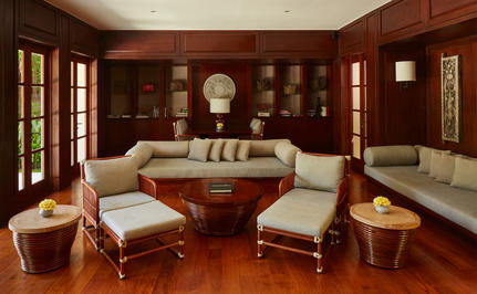 Principal bedroom at Aman Villas at Nusa Dua with warm wood panelling, cream armchairs and a draped bed.