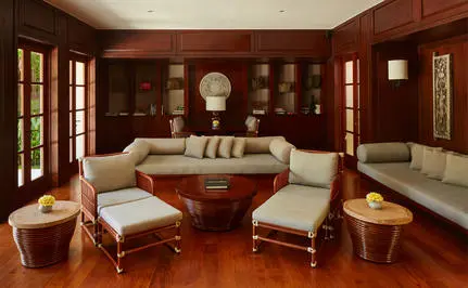 Principal bedroom at Aman Villas at Nusa Dua with warm wood panelling, cream armchairs and a draped bed.