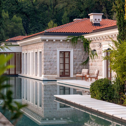 Waterfront pavilion at Aman Sveti Stefan with classical columns and terracotta roof reflected in still water.