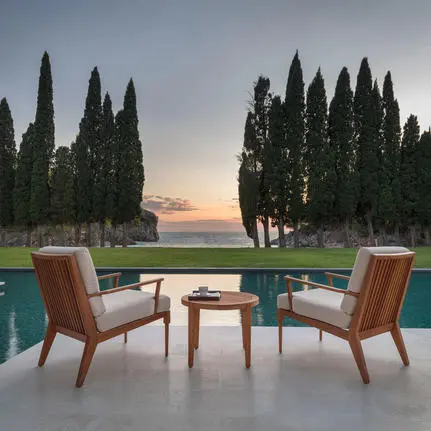 Two mid-century chairs beside a wooden table on a terrace overlooking a pool and cypress trees at sunset, Aman Sveti Stefan.