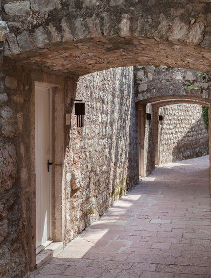 Stone corridor with weathered arches at Aman Sveti Stefan, morning light casting shadows on aged walls.