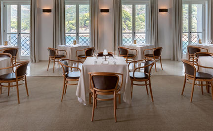 Dining room at Aman Sveti Stefan with wooden chairs and tables beside tall windows.