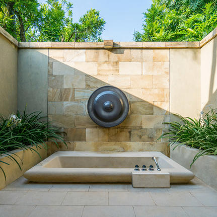Outdoor bathtub with circular water feature at Amanjiwo resort, framed by stone walls and green foliage.