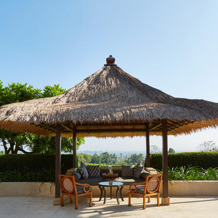 Pavillon au toit de chaume avec mobilier en bois au resort Amanjiwo, vue sur la vallée