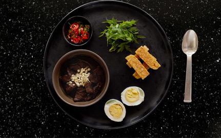 Amanjiwo dining experience: soup bowl with garnish, fresh herbs, citrus slices, and breadsticks arranged on dark plate.