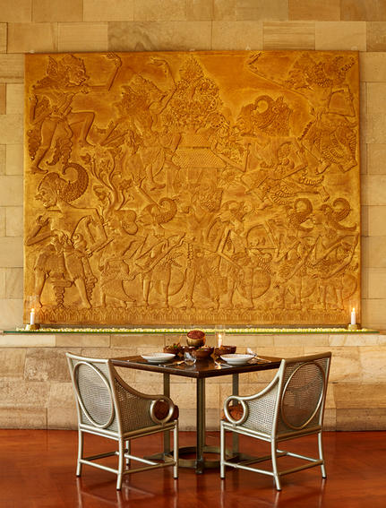 Circular dining table with two chairs beneath a large golden abstract artwork at Amanjiwo.