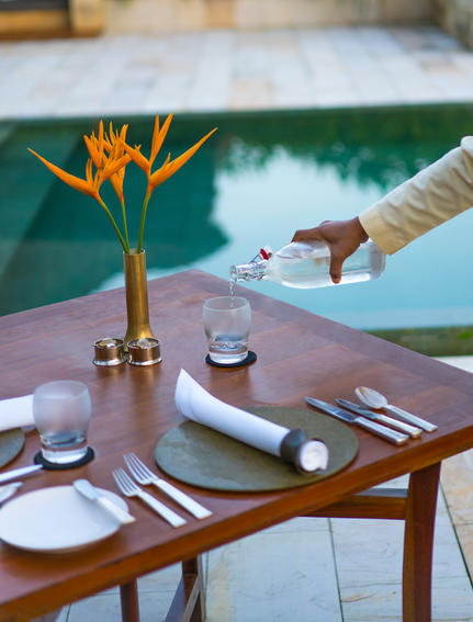 Dining table set with place settings and bird of paradise flower, overlooking pool at Amanjiwo.