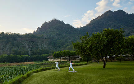 Two guests seated on the lawn at Amanjiwo, with verdant rice terraces and forested mountains beyond.