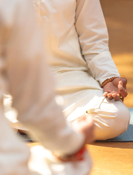 Mains posées en méditation, vêtues de blanc, à la station balnéaire Amanjiwo.