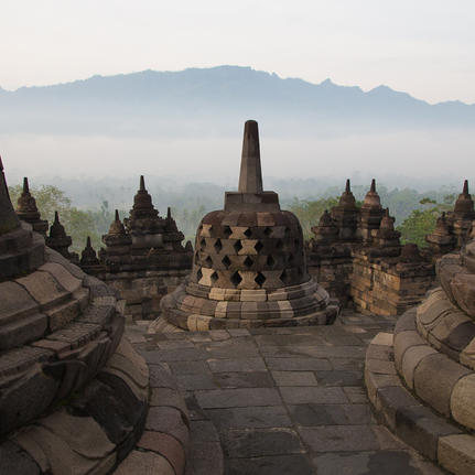 Stone stupas at Amanjiwo with misty volcanic peaks beyond, Java, Indonesia.