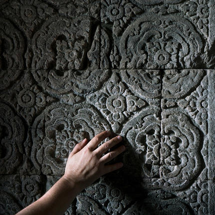 Hand touching ornate carved stone detail at Amanjiwo.