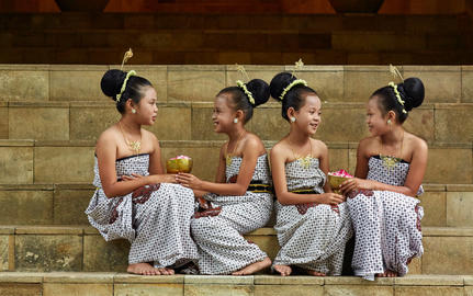 Four Balinese dancers in traditional dress sit together on stone steps at Amanjiwo resort.