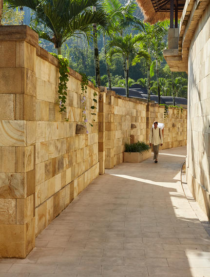 Corridor pavée bordée de murs en pierre avec végétation tropicale, Amanjiwo resort.