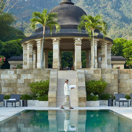 Amanjiwo's domed pavilion reflected in a still pool, framed by columns and tropical palms against verdant hillsides.