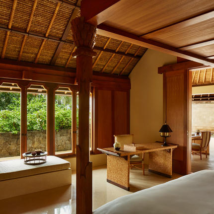 Balinese-style principal bedroom with wooden beams and pillars at Amankila resort, featuring large windows overlooking tropical gardens.