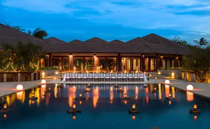 Amanpulo's dining venue illuminated at dusk, reflected in still water with mountain backdrop.