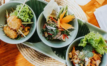 Tres platos con ensaladas frescas y proteínas en la sala de comedor de Amanpuri.
