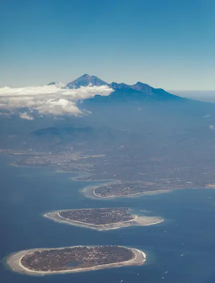 Aerial view of Amanwana's island setting, with volcanic mountain rising above clouds and surrounding turquoise waters.