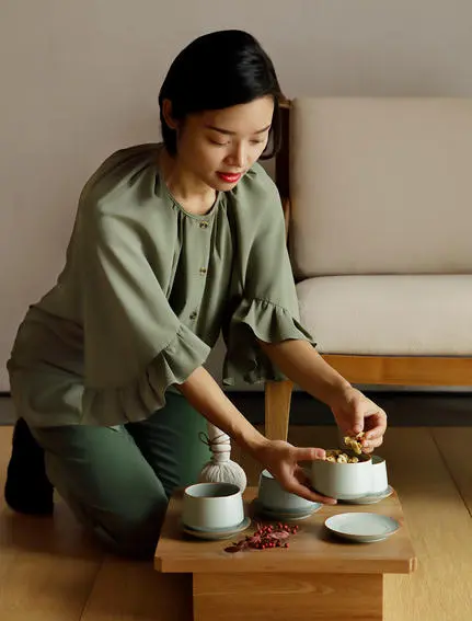 养云安缦度假村内,一位女性穿着绿色外套跪坐在木制茶盘前,专注地进行茶艺表演。