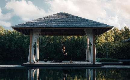 Geometric pavilion reflected in still water at Amanyara, surrounded by tropical vegetation.