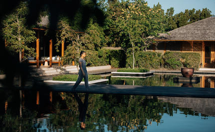 Infinity pool reflecting surrounding trees at Amanyara, with thatched-roof pavilions beyond.