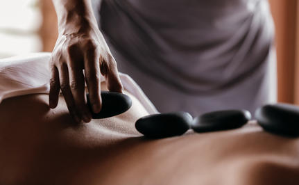 Therapist's hands placing heated stones on a guest's back during a wellness treatment at Amanyara.