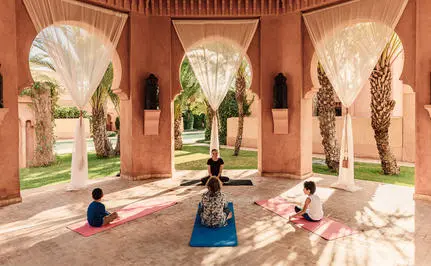 Family enjoying yoga session in Amanjena's terracotta-coloured courtyard with arched doorways.