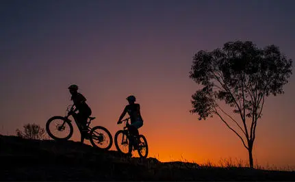Family cycling at sunset at Amanjena, silhouetted against an orange sky.