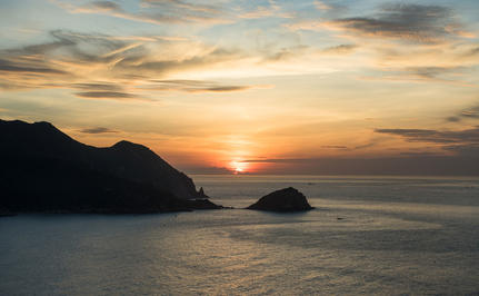 安缦诺怡度假村海岸线上，夕阳西下映照在平静海面，远处山峦轮廓清晰。