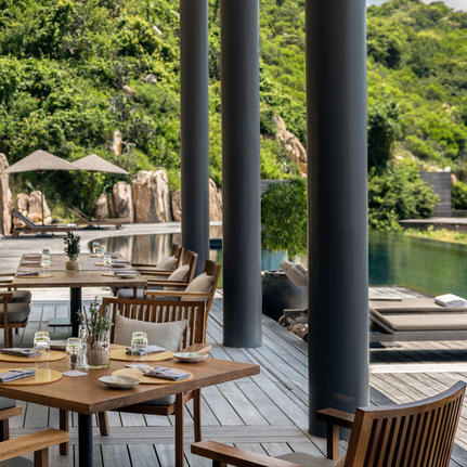 Wooden deck at Amanoi with dining furniture and water views through supporting columns.