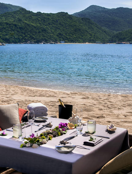 Beachfront dining setup at Amanoi with turquoise waters and forested hills beyond.