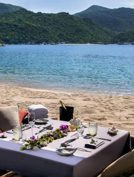 Beachfront dining setup at Amanoi with turquoise waters and forested hills beyond.