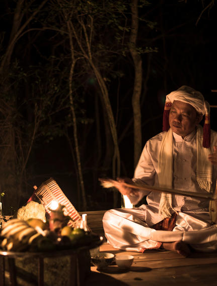 Woman seated by candlelit campfire at Amanoi, reading by firelight at night.