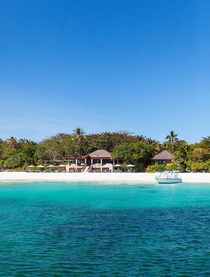 安缦璞乐度假村海滨景观，白沙滩与翠绿植被相映，清澈蓝绿色海水在前。