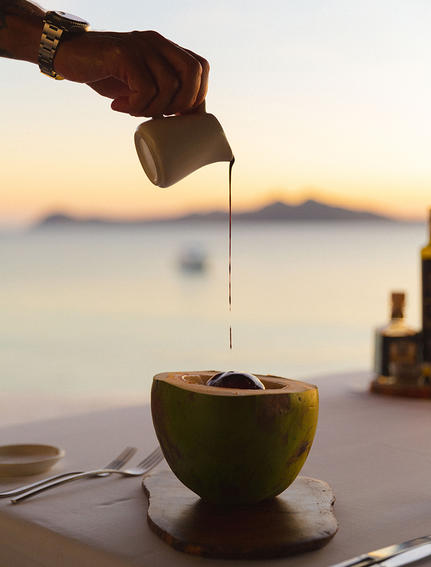 安缦璞乐度假村，手倒果汁入椰子杯，背景为晨雾笼罩的海景。