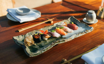 Sushi platter at Nama dining venue, Amanpuri, with ceramic plates and small sauce dish on wooden table.