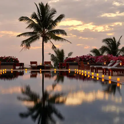 Amanpuri resort at dusk, with palm trees reflected in still waters and warm lights glowing along the waterfront.