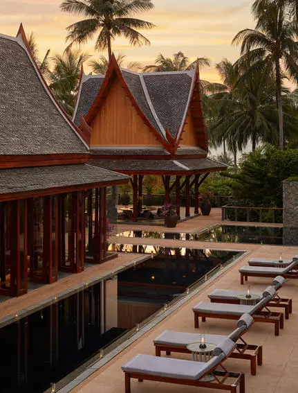 Amanpuri resort dining pavilion at sunset, with wooden tables set beside palm trees and traditional Thai architecture.