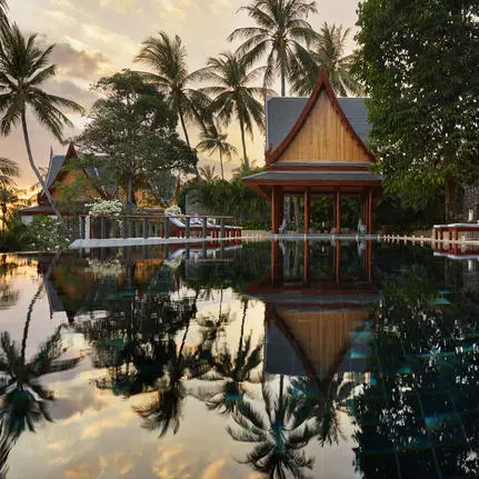 Thai sala reflected in still water at Amanpuri resort, surrounded by palm trees at dusk.