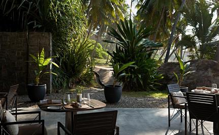 Amanwella's dining venue with stone terrace, dark tables and chairs, and lush tropical greenery surrounding the space.