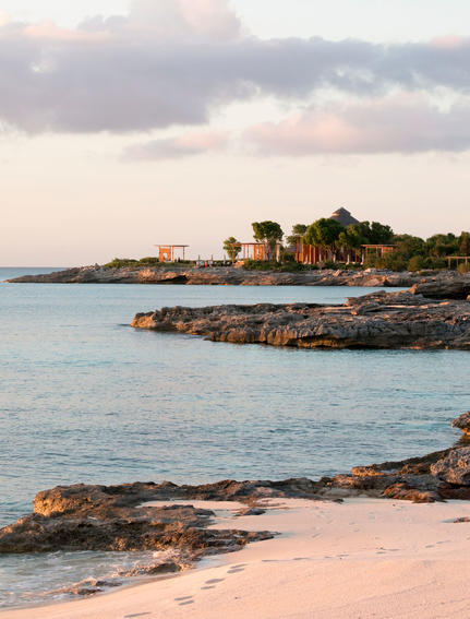 Côte rocheuse d'Amanyara avec plage de sable rose et eaux turquoise au crépuscule.