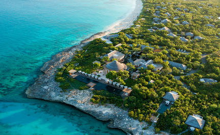 Aerial view of Amanyara resort nestled on a turquoise coastline, with white villas scattered amongst dense tropical vegetation.