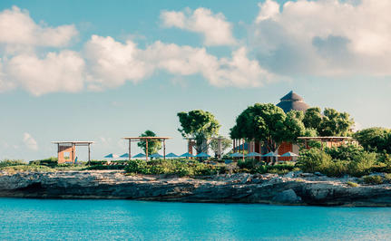 Amanyara resort nestled on a turquoise lagoon with palm trees and waterfront buildings under a cloudy sky.