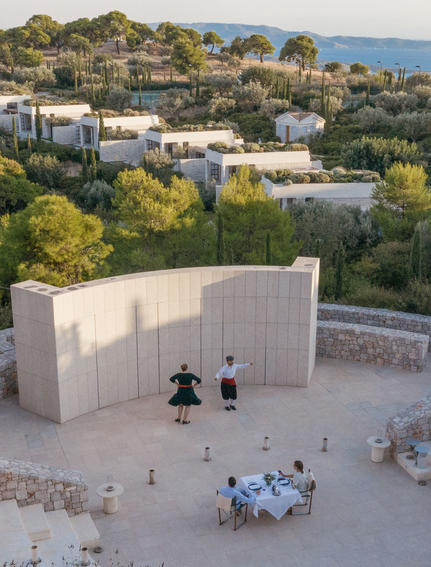 Aerial view of Amanzoe's contemporary pavilion with guests gathered in the courtyard, surrounded by Mediterranean landscape and sea views.
