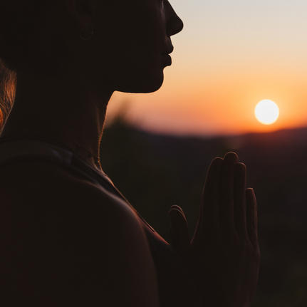 Silhouetted figure gazing towards sunset at Amanzoe, golden light reflecting on skin against darkening sky.
