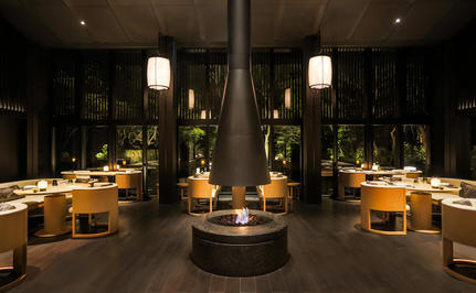 安缦京都度假村内部餐厅,夜间照明营造温暖氛围,中央火炉两侧排列金色灯具。