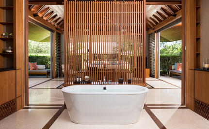Bathroom in a four-bedroom beach sala villa at Amanyara resort, featuring a freestanding white bathtub and wooden architectural details.