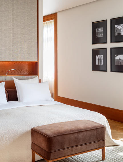 Principal bedroom at Aman Sveti Stefan with sea views, featuring wooden-framed bed and suede ottoman.