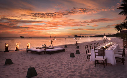 Beach barbecue setup at sunset with dining tables and boat at Amanpulo.