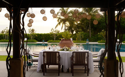 Covered dining pavilion at Amanpulo with poolside seating and tropical gardens beyond.
